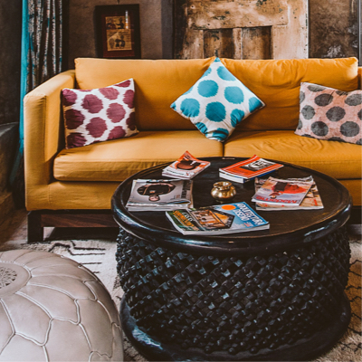 A beige couch with multiple coloured pillows behind a round table topped with books